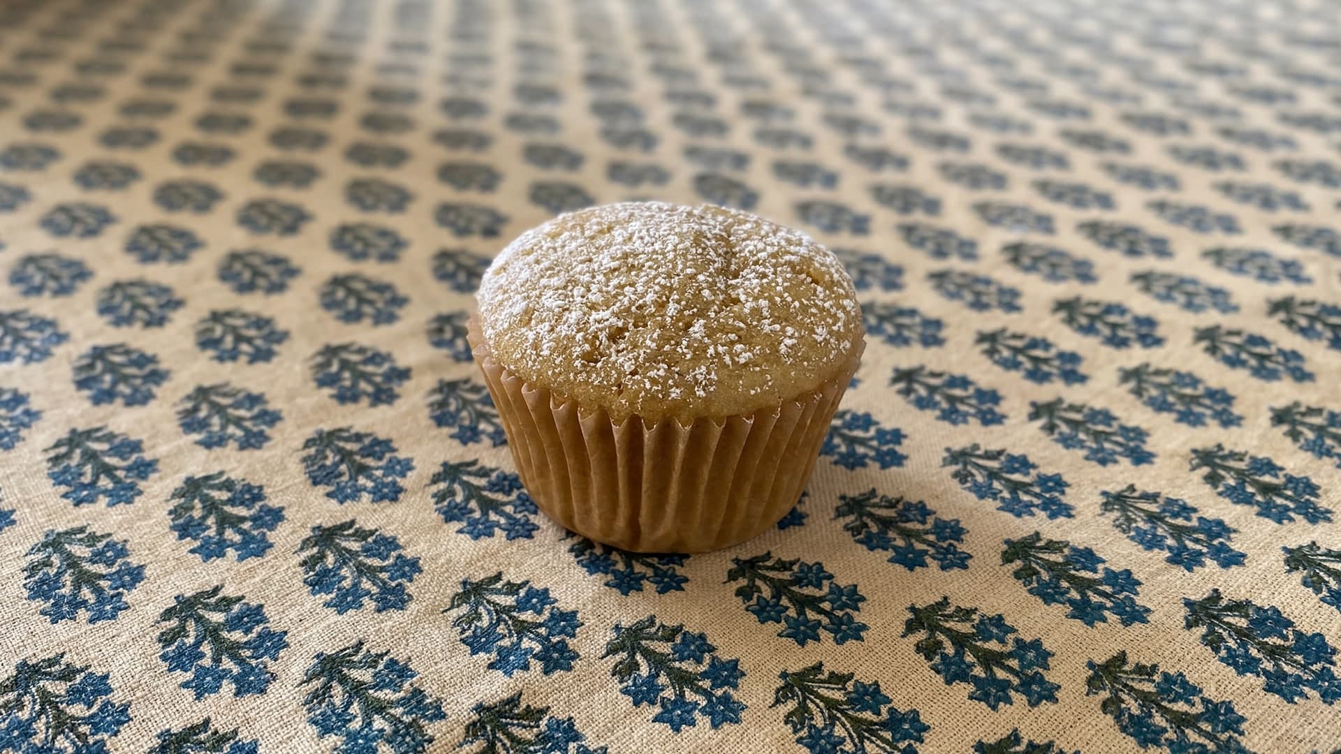 Casual phone-style photo of a strawberry muffin on a printed tablecloth.